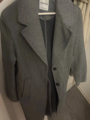 Grå kappa från Bershka - Stilren grå kappa från Bershka i ullblandning. Klassisk rak modell och perfekt för kyliga dagar. Den är i storlek S men passar även xs och M