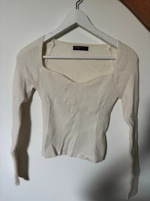 Vit ribbad stickad topp  - Trendig vit ribbad stickad topp från SHEIN med lång ärm och fyrkantig urringning. Figurnära passform och dekorativa sömmar framtill ger en snygg siluett. Perfekt att matcha med jeans eller kjol för en clean look.