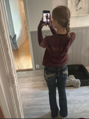 Mörkblå bootcut jeans med brodyr - Säljer ett par mörkblå bootcut jeans med vita kontrastsömmar och snygg brodyr på bakfickorna. Jeansen har låg midja och klassisk femficksdesign. Perfekta för dig som gillar en avslappnad men ändå trendig stil.