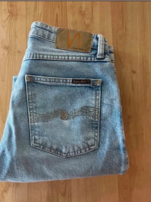 Nudie jeans  - Säljer ett par ljusblå jeans från Nudie Jeans med klassisk femficksmodell och raka ben. Jeansen har en rå, fransad kant nedtill och är tillverkade i bomull.Snygg broderad detalj på bakfickan och Nudie-logga på läderpatchen bak.Midja 35, längd 96cmJAG SKICKAR EJ FLER BILDER NÄR JAG BÄR JEANSEN! för bättre inblick i passformen rekommenderar jag att googla på modellnamnet. För storleksguide kolla måtten noggrant då jeansen alltid kan vara uppsydda heller krympta och jag ej tar emot returer :) (n8)