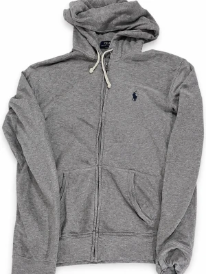 Polo Ralph Lauren grå zip hoodie – XS - 🩶 Klassisk Polo Ralph Lauren zip hoodie i gråmelerad färg med den ikoniska mörkblå Polo-loggan på bröstet.  ✨ Stilren och tidlös modell 🔹 Full zip framtill 🔹 Broderad Ralph Lauren-logo 🔹 Huva med dragsko 🔹 Två fickor framtill 🔹 Storlek XS 🔹 Lätt att styla året runt – perfekt med jeans, chinos eller sweatpants  📦 Snabb frakt 💬 Skriv gärna vid frågor eller om du vill ha mått 💸 Öppen för rimliga bud 👕 Fler märkesplagg finns på profilen – samfraktar gärna!