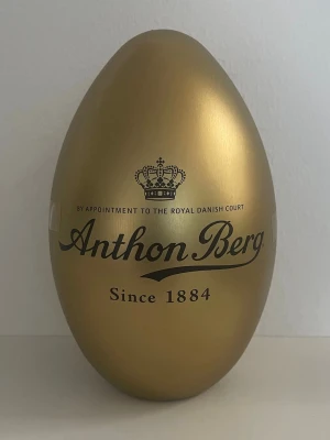 Guldägg från Anthon Berg - Säljer ett stort guldägg från Anthon Berg, känt för sina exklusiva chokladprodukter. Ägget är gyllene och har elegant svart text med logga och krona. Perfekt som present eller dekoration till påsk.