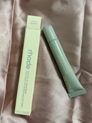 Rhode Peptide Lip Treatment Salted Caramel - Rhode Peptide Lip Treatment i doften Salted Caramel. Kommer i en stilren, ljusgrå tub med matchande förpackning. Innehåller 10 ml och är designad för att återfukta och vårda läpparna med peptider. Perfekt för dig som vill ha mjuka och återfuktade läppar.