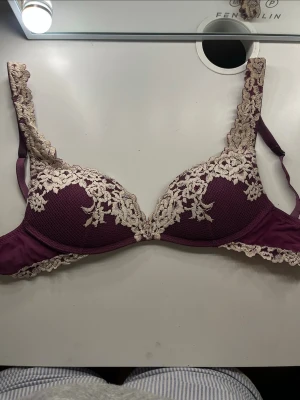 Lila Intimissimi-bh med spetsdetaljer - Snygg lila push-up bh med vadderade kupor och vacker beige spets längs kanterna och axelbanden. Bh:n har en design med blommiga spetsmönster och justerbara axelband. Den har lite defekter bland annat mellan kuporna där tyget sprucket lite (finns bild). Säljer då den är för liten på mig! Bilderna är från plick då jag köpte den där, jag har bara använt den 3 gånger dock🥰