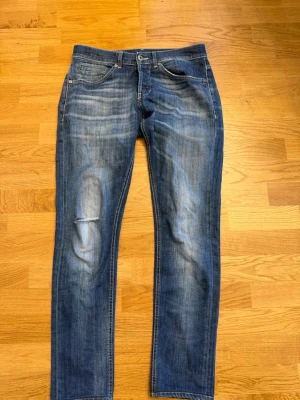 Blå slitna dondup jeans med raka ben - Säljer ett par blå jeans med raka ben och slitningar på låret. Jeansen har klassisk femficksdesign och kontrastsömmar. Materialet är denim i bomull och passformen är normal. Perfekta för en avslappnad look.
