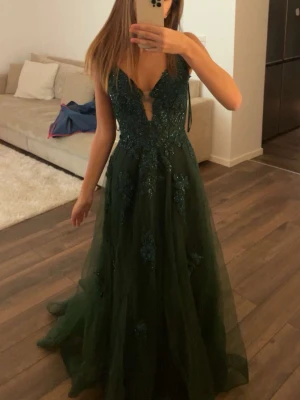 Balklänning  - Säljer en elegant mörkgrön långklänning med v-ringning, spetsdetaljer och snörning i ryggen. Klänningen har ett lager av tunn tyll och vackra broderade blommor på överdelen. Perfekt för bal 🩷den är i storlek xs