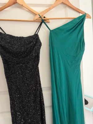 Svart glittrig långklänning & grön långklänning  - Säljer en svart långklänning med glittriga paljetter och smala axelband. Klänningen har en elegant slits framtill och sitter tight för en snygg siluett. Perfekt för dig som vill sticka ut på festen!