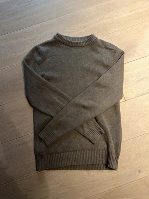 Olivgrön stickad tröja - En enkel och stilren ljus brun stickad tröja med rund halsringning och ribbade muddar vid ärmslut och nederkant. Perfekt för lager på lager och passar till det mesta. Materialet känns mjukt och bekvämt.