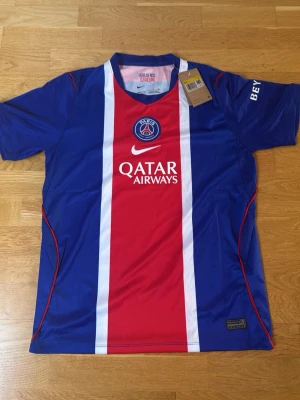 PSG matchtröja Nike blå/röd - Säljer en officiell Paris Saint-Germain matchtröja från Nike i blått och rött med vita detaljer. Tröjan har klubbmärke och Qatar Airways-tryck på bröstet samt Dri-FIT-material som andas. Perfekt för fotbollsträning eller att bära på läktaren.
