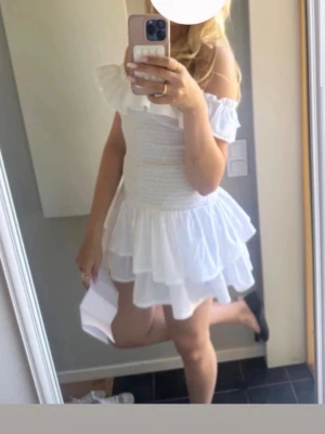 Vit offshoulder volangklänning - Supersöt vit kortklänning med offshoulder och volanger. Klänningen har smockad överdel och dubbla lager i kjolen för extra volym. Perfekt för sommarens alla tillfällen! Jag har endast haft på mig den på min konfirmation så den är helt ny. Man måste inte heller ha off shoulder om man it vill!         Nypris 399 