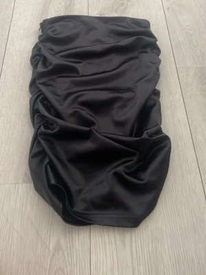 Svart satin kjol från SHEIN - Snygg svart kjol från SHEIN i glansigt satinmaterial. Kjolen har en åtsittande passform och är draperad för en trendig look. Perfekt för dig som gillar stilrena och moderna plagg.