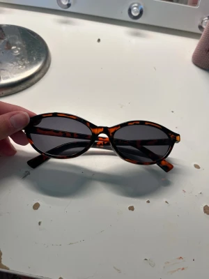  solglasögon - Snygga ovala solglasögon med leopardmönstrad båge i brunt och svart. Glasen är mörka och ger en cool retrovibe. Perfekta för att lyfta vilken outfit som helst och ge en trendig touch till din stil.