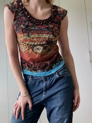 Flerfärgad mönstrad Y2k topp - Unik topp med många detaljer och fina mönster runt om. Lättsamt material som sätter sig snyggt runt kroppen. Jeansen säljs också separat!