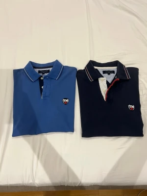 2 pikétröjor från Tommy Hilfiger - Två snygga pikétröjor från Tommy Hilfiger i storlek L. En är blå med vita och svarta detaljer, den andra är mörkblå med vit och röd knappslå. Båda har klassisk krage, knappar och logga på bröstet. Perfekta för en stilren och sportig look. De kostar endast 200kr styck vill man köpa båda så kostar det 350kr. Kontakta mig bara om vilken tröja ni vill ha eller om ni vill ha båda.