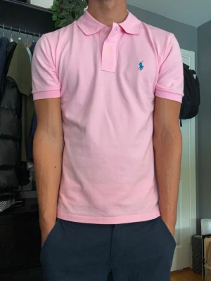 Ralph Lauren Piké – Ljusrosa - Säljer en klassisk Ralph Lauren piké i en snygg ljusrosa färg med turkos broderad logga. En perfekt piké för sommaren eller en stilren vardagslook. Den är aldrig använd så skicket är som nytt. Storleken är Small och sitter ganska true to size, om något är den lite stor i storleken. 