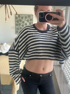 Randig croppad stickad tröja - Säljer en croppad stickad tröja med svarta och vita horisontella ränder. Tröjan har breda ärmar, rund halsringning och är gjord i ett mjukt, fluffigt material. Perfekt för dig som gillar en avslappnad och trendig stil. Pris kan diskuteras. 