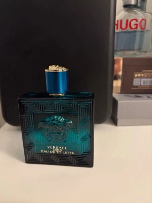 Versace Eros Eau de Toilette - Sprutade Max 5-15 gånger. Versace Eros Eau de Toilette i en stilren, fyrkantig flaska av blått glas med gulddetaljer och Medusa-huvud i relief på framsidan. Flaskan har ett elegant mönster och blått lock med guldkant. Perfekt för dig som gillar exklusiva dofter.