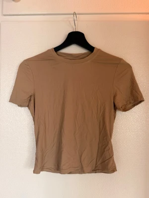 Beige croppad t-shirt - En enkel och stilren beige t-shirt med croppad passform och rund hals. T-shirten har korta ärmar och är tillverkad i ett mjukt material som känns skönt mot huden. Perfekt att matcha med jeans eller kjol för en clean look.