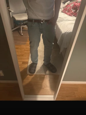 Levis 511 ljusblå jeans - Säljer ett par ljusblå jeans med rak passform och klassisk femficksdesign. Jeansen har en normal midja och medföljer ett brunt flätat bälte. Perfekta för en avslappnad och stilren look. Materialet är denim i bomull. W30 L32
