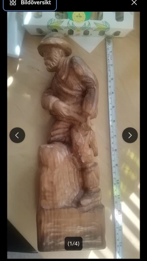 Handsnidad träfigur soldat - Unik handsnidad träfigur som föreställer en soldat med hjälm och väska, stående mot en stubbe. Figuren är gjord i ljust trä med tydliga snidardetaljer och mäter cirka 30 cm i höjd. Perfekt som dekoration eller samlarobjekt.