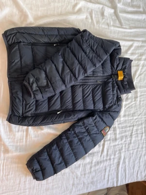Svart dunjacka från Parajumpers - Snygg svart dunjacka från Parajumpers med lättviktsdesign. Jackan har två dragkedjefickor framtill, hög krage och klassisk patch på ärmen. Perfekt för alla tillfällen och enkel att bära tack vare den lätta konstruktionen. PRIS GÅR ATT DISKUTERA 
