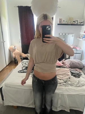 Beige croppad topp med resår - Säljer en beige croppad topp med resår i midjan och lös passform upptill. Toppen är kortärmad och har en mjuk, sammetsliknande känsla. Pris går att diskuteras