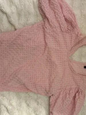 Ljusrosa topp med puffärm - Supersöt ljusrosa topp med puffärmar och strukturerat tyg. Toppen har rund halsringning och är tillverkad i ett lätt material som passar perfekt till vår och sommar. Enkel men ändå trendig design som är lätt att matcha.