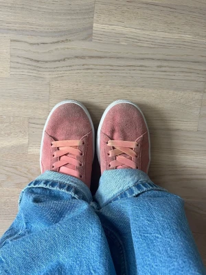 Puma sneakers med rosett - Snygga orangea/rosa Puma sneakers i ett mockaliknande material med stora satinrosetter baktill och matchande band som skosnören🩷🧡 Skorna har vit sula och klassisk Puma-logga i guld på sidan. Jättecool detalj i en outfit! Köpta på en outlet i London.