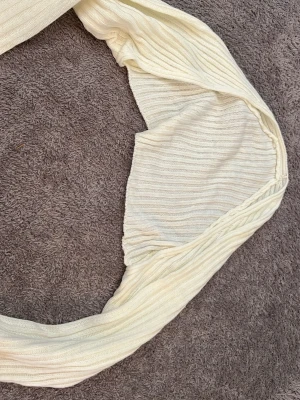 Krämvit ribbad halsduk - Säljer en krämvit kofta i ribbstickat material.  Koftan är lång och mjuk med en enkel, stilren design som passar till det mesta.