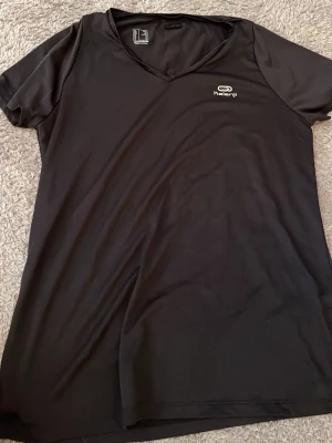 Svart v-ringad t-shirt från Kalenji - Säljer en svart t-shirt från Kalenji med v-ringning och korta ärmar. Perfekt för träning med sitt lätta och snabbtorkande material. Diskret logga på bröstet och enkel, stilren design som passar till det mesta.