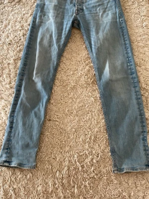 Ljusblå Jack and Jones tapered jeans - Säljer ett par ljusblå Jack and Jones jeans med rak passform och klassisk femficksdesign. Jeansen har normal midja och stängs med knappar. Perfekta till en avslappnad stil och passar till det mesta i garderoben.