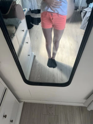 Neonrosa jeansshorts med rå kant - Säljer ett par neonrosa jeansshorts med rå kant nertill och klassisk femficksdesign. Shortsen har knapp- och dragkedjestängning samt bälteshällor. Perfekta för sommaren och ger en färgstark look.
