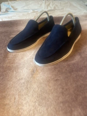 Mörkblå mockaloafers med vit sula - Snygga mörkblå loafers i mocka med stilren design och vit, platt gummisula. Skorna har en klassisk slip-on modell utan snörning och passar perfekt till en avslappnad men ändå uppklädd look. Perfekta för dig som gillar enkel och modern stil. Nypris 800 mitt pris 650