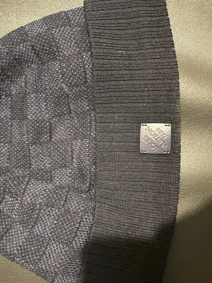 Blå Louis Vuitton Neo Petit Damier Mössa - Snygg blå stickad mössa från Louis Vuitton med diskret rutmönster och ribbad kant. Mössan har en metallbricka med Louis Vuitton-logga framtill. Perfekt accessoar för kyliga dagar och en stilren look. Nypris:3800kr                                                  Använd ett fåtal gånger‼️Skriv om ni har några funderingar eller frågor! Priset är fastställt. 