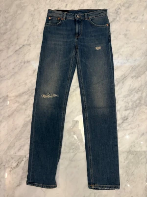 Dondup jeans - Säljer ett par klassiska blå jeans från Dondup med raka ben och slitningar på låret och vid fickan. Jeansen har fem fickor, gylf med knapp och dragkedja samt snygga kontrastsömmar. Tillverkade i denim med en cool vintagekänsla. Strl 12 men sitter som 28-29