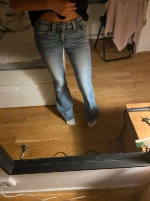 Blå bootcut jeans med låg midja - Säljer ett par blå bootcut jeans med låg midja och klassisk femficksmodell. Jeansen har en snygg tvätt med lätt slitning och är tillverkade i ett mjukt denimtyg. Perfekta för en avslappnad och trendig look. Lite sönder trampade ner till men inget som märks.