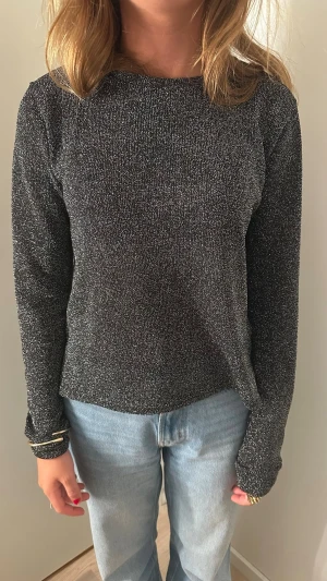 Glittrig svart långärmad tröja - Snygg svart långärmad tröja med glittrig finish. Tröjan har en rak passform och rund halsringning. Perfekt för dig som vill ha något extra till din outfit.