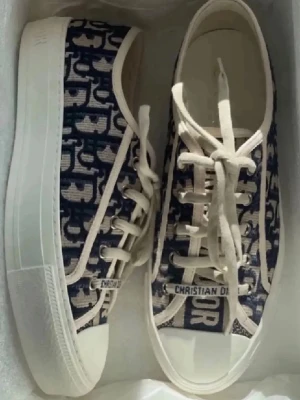Christian Dior blåvita sneakers - Snygga sneakers från Christian Dior i blått och vitt med tydligt logomönster. Skorna har vita snören, gummisula och canvasmaterial. Klassisk låg modell med rund tå och märkning på plösen och snörningen. Perfekta för en trendig streetstyle-look.  KVITTO FINNS!!