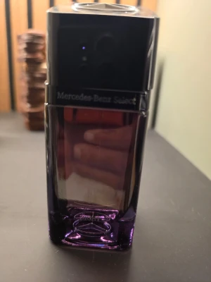 Mercedes-Benz Select parfym - En stilren parfymflaska från Mercedes-Benz Select med elegant svart och mörklila glas. Flaskan har en fyrkantig form och en modern design som känns lyxig och exklusiv. Perfekt för dig som gillar snygga detaljer på parfymhyllan.