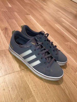 Adidas Sneakers - Säljer ett par använda grå sneakers från Adidas. Skorna har grå snören gul-brun sula. Skorna är använda ett par ggr men har inga tydliga tecken på användning, så funkar lika bra o använda flera ggr till.