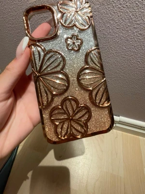 Glittrigt mobilskal med blommor - Snyggt mobilskal i guld och silver med glittrig finish och upphöjda blommor i metallic. Skalets design är trendig och sticker ut med sina stora blommor och skimrande yta. Passar perfekt för dig som vill ha ett unikt och stilrent skydd till mobilen. Passar till en IPhone 11 och en XR. 