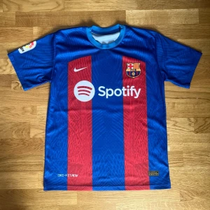 FC Barcelona matchtröja Lewandowski - Säljer en officiell FC Barcelona matchtröja från Nike med Lewandowski och nummer 9 på ryggen. Tröjan är blå och röd med klubbmärke, Nike-logga och Spotify som sponsor framtill. Tillverkad i lätt funktionsmaterial med korta ärmar och rund hals.