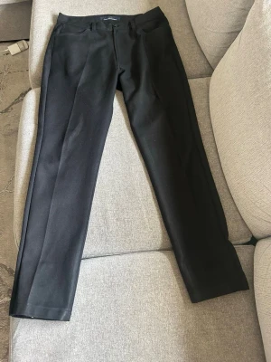Svarta kostymbyxor från Jeff Company - Snygga svarta kostymbyxor från Jeff Company med raka ben och klassisk passform. Byxorna har bälteshällor, knapp och dragkedja framtill. Perfekta till en stilren look och passar till många olika outfits.