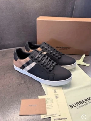 Burberry sneakers med rutigt mönster - Snygga sneakers från Burberry i svart och beige med klassiskt rutigt mönster på sidan. Skorna har vita sulor och svarta skosnören. Tillverkade i läder och textil för en exklusiv känsla. Perfekta för dig som vill ha en stilren och trendig look.