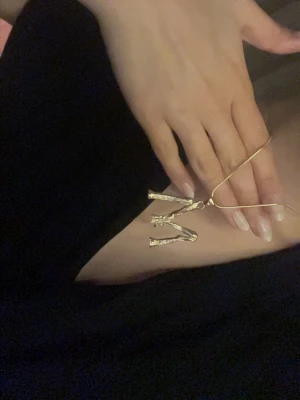 Guldigt halsband med bokstaven M - Säljer ett halsband med ett stort, guldigt M-hänge i en rå, grenliknande design. Kedjan är tunn och matchar hängets färg.💕
