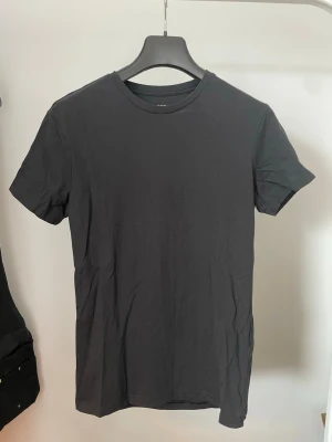 Svart t-shirt från Pier One XS - En enkel och stilren svart t-shirt från Pier One i storlek XS. T-shirten har rund halsringning och korta ärmar. Tillverkad i mjuk bomull som känns skön mot huden. Perfekt basplagg till garderoben.