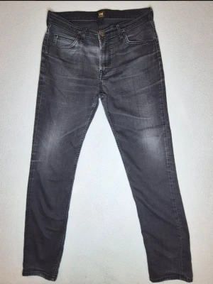Lee Rider jeans svarta/grå W33 L32 slim straight denim - Lee Rider jeans i gråsvart/svart tvätt.  Klassisk 5-ficksmodell med knapp, dragkedja, bälteshällor och Lee-detaljer.  Snygga vardagsjeans som funkar till både t-shirt, hoodie och skjorta.  Märke: Lee Modell: Rider Storlek: W33 L32 Färg: Gråsvart/svart denim