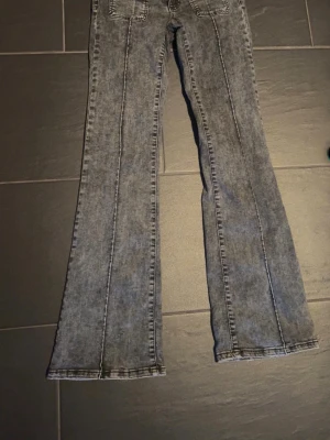 Grå bootcut jeans med tvättad look - Säljer ett par grå bootcut jeans med tvättad effekt och markerade sömmar. Jeansen har fickor både fram och bak samt utsvängda ben. Perfekta för dig som gillar retrostil och vill ha ett par snygga jeans med unik finish.  Jeans ifrån Nelly använda 1-2 gånger så väldigt bra skick. Storlek: 34 