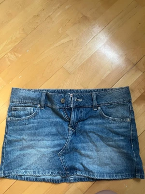 Blå jeanskjol i kort modell - Säljer en klassisk blå jeanskjol i kort modell, Kjolen har en rak passform och är tillverkad i slitstarkt denimtyg. Perfekt till sneakers eller boots för en avslappnad look. Kjolen är endast använd en gång, köpte på Gina på Valborg!