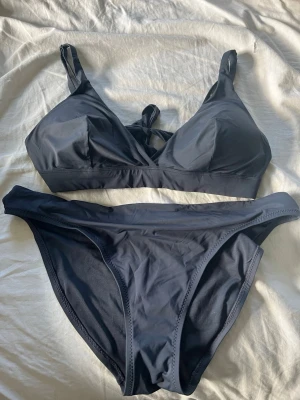 Mörkblå bikini med knyt framtill - Snygg mörkblå bikini med enkel design och knyt framtill på toppen. Både överdel och underdel har en klassisk passform och är tillverkade i ett mjukt, stretchigt material som passar perfekt för lata dagar på stranden.